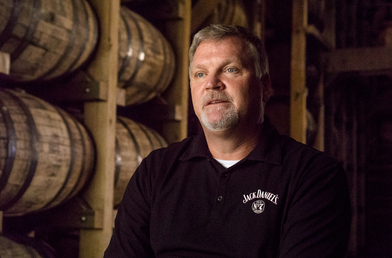 Man in Jack Daniels shirt in front of whiskey barrels