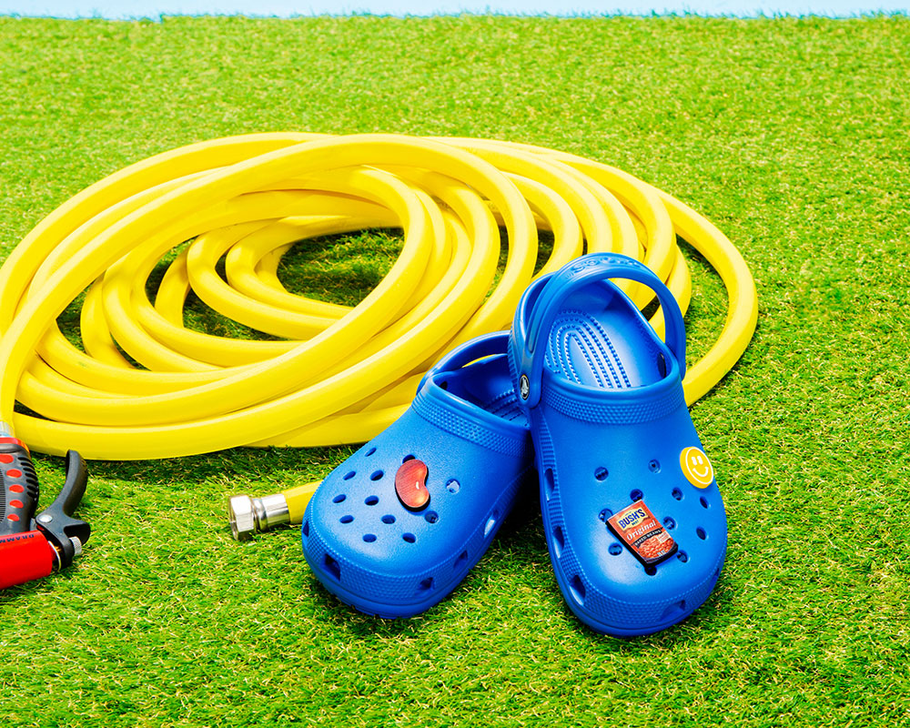 Yellow hose and blue crocs on grass. The crocs have bean jibbitz on them.