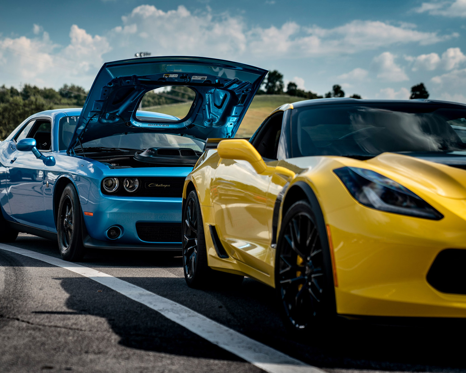 Yellow car in foreground, blue car in background with hood up.