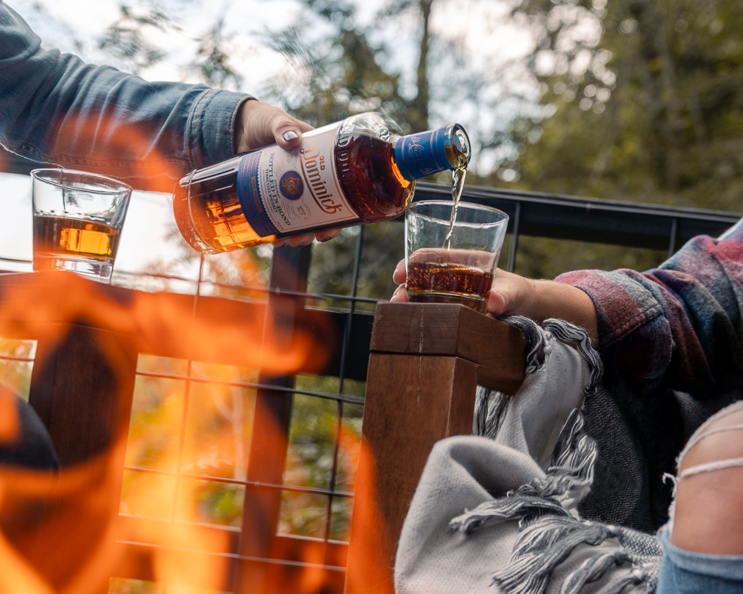 Friends pouring ODD whiskey outside by a fire.