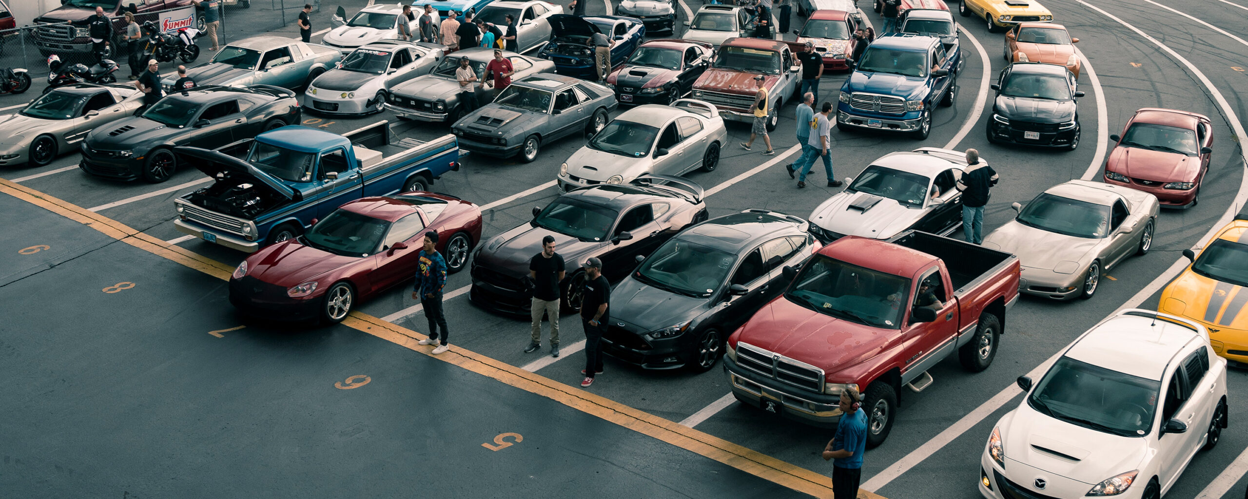 People walking around cars in lanes for a race.