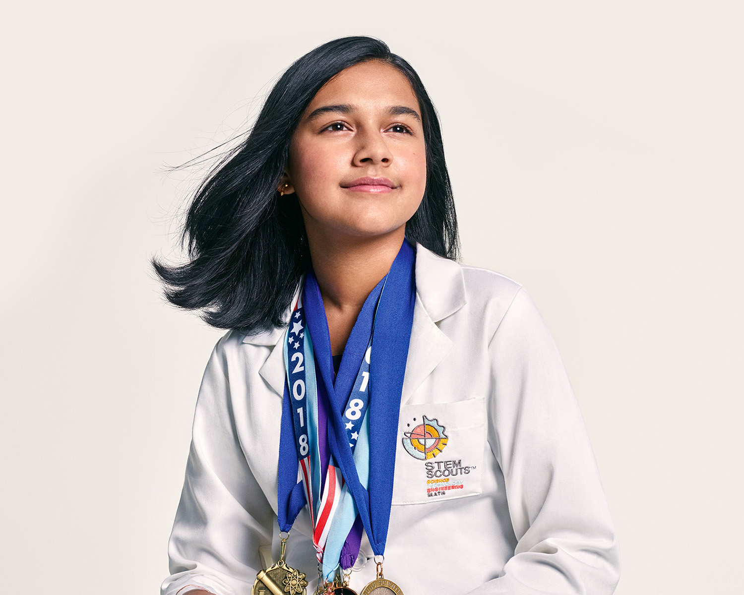 Girl wearing STEM lab coat and several medals.